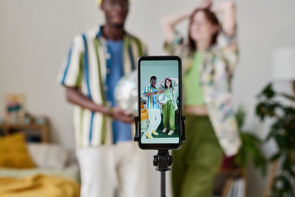 To ungdommer, en jente og en gutt, poserer foran en et mobilkamera på stativ.